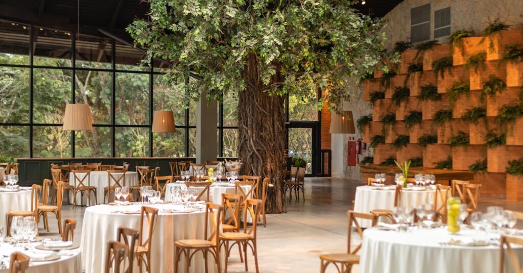 Chic dining area in a hall with elegant table settings surrounded by greenery and trees.